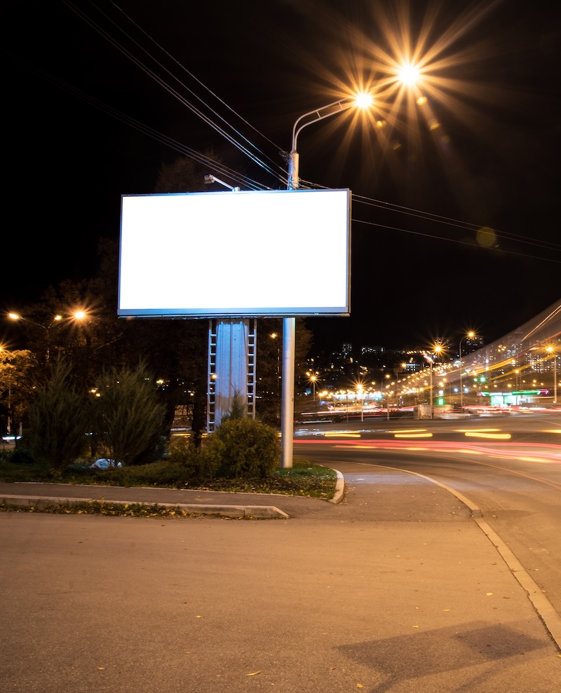 Noćni outdoor — LED billboard uz cestu, svjetlosni tragovi vozila i grad u daljini